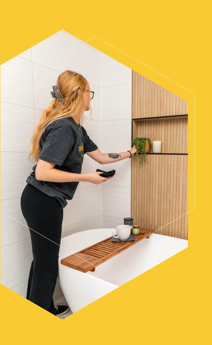 A professional cleaner from Clean Bees Homekeepers meticulously adjusts a plant and decorative items on a clean bathroom countertop, showcasing the attention to detail in our bathroom cleaning services in Fort Collins.