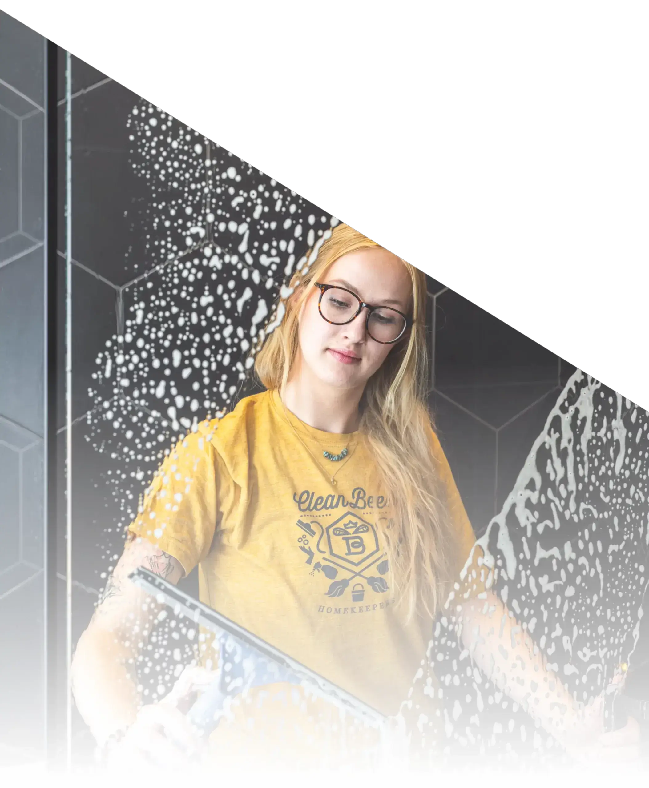 A professional cleaner from Clean Bees Homekeepers using a squeegee to clean a glass shower door, showcasing our meticulous glass cleaning services.